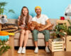 Positive delighted woman and man play with their favourite dog, pose on sofa, rejoice day of moving in new apartment, surrounded with different boxes, indoor plants. Family, relocation and fun concept